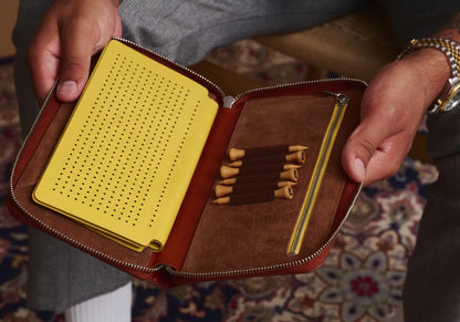 Brown leather case with yellow interior, containing small items, held by a person.